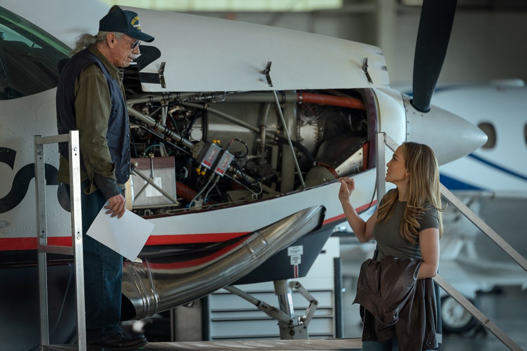 "A man and a woman discuss beside an aircraft with its engine exposed inside a hangar, suggesting a maintenance or technical check setting."